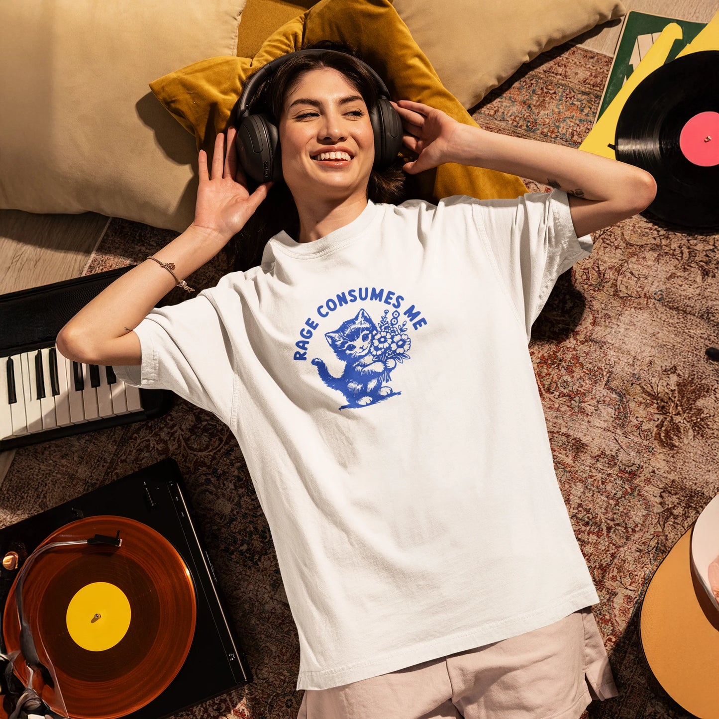 Person wearing headphones and a t-shirt with a graphic design, lying on a carpeted floor with musical instruments around.